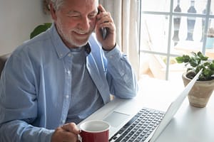 Senior light skinned businessman working on laptop computer using cellphone