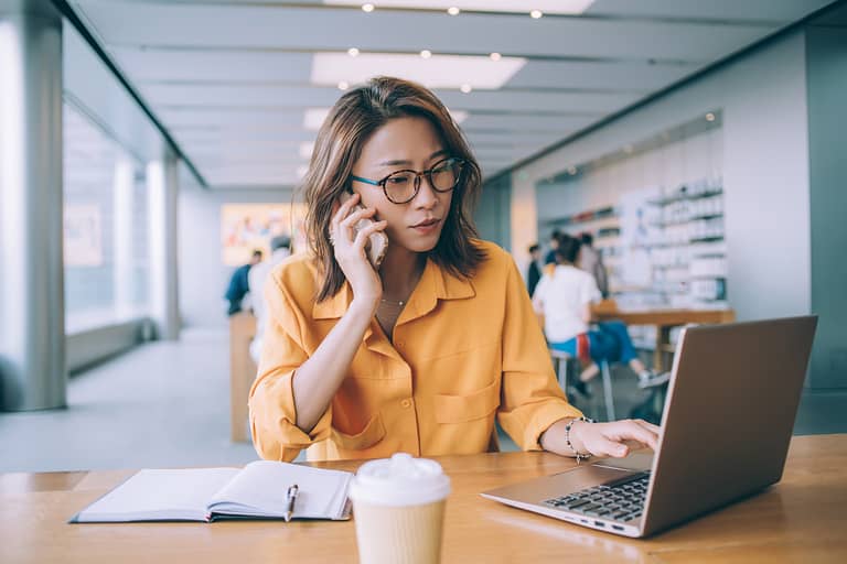 woman in trendy spectacles talking on the phone & using her laptop