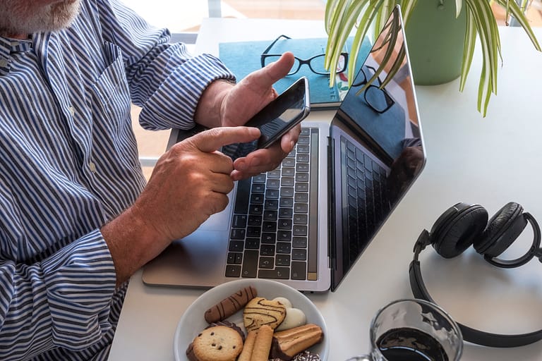 A senior man with beard using cellphone and laptop