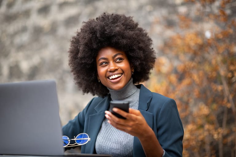 happy business woman sitting outside with laptop and mobile phone
