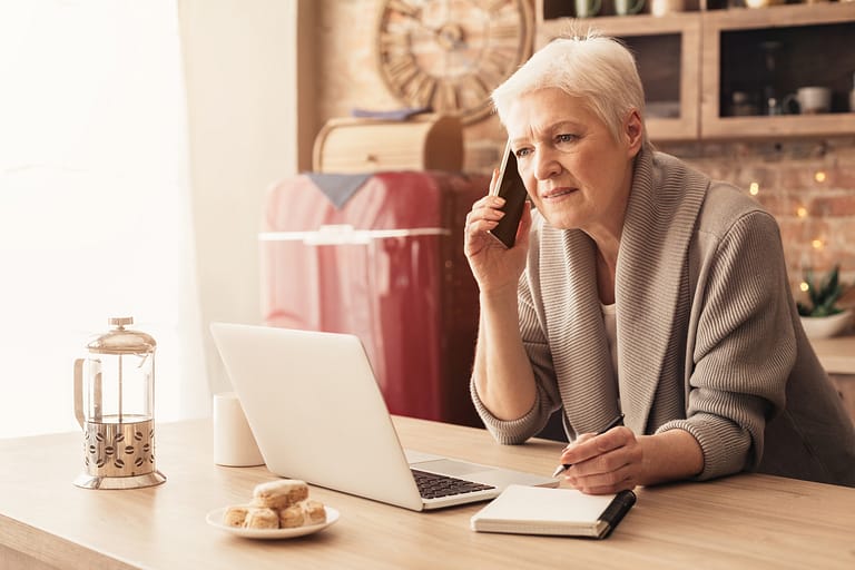 Senior Businesswoman Using Laptop, Talking On Cellphone And Taking Notes